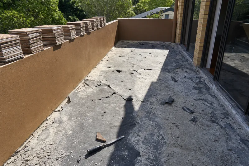 A balcony stripped wall to wall, perished black membrane peeling away from the concrete slab and removed tiles stacked on the balustrade wall — illustrative example